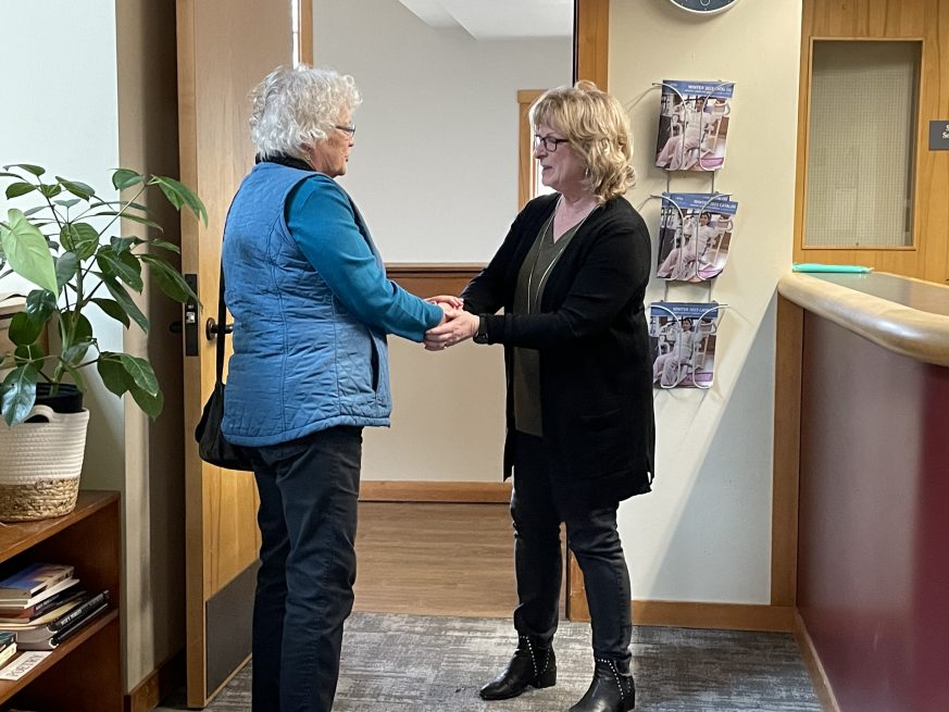 Photo of two people in an office setting, facing each other and clasping hands in front of an open door