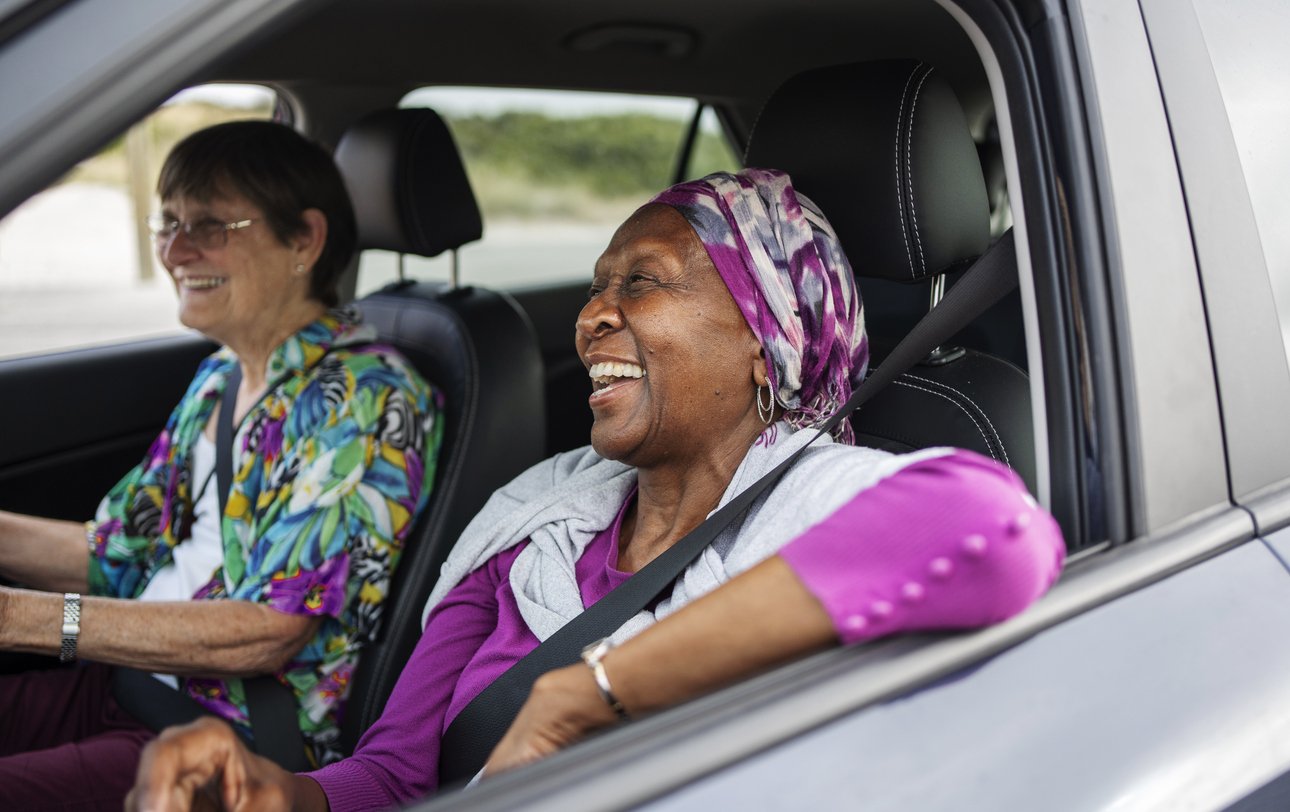 Senior women laughing while sitting in the passenger seat of a car during a road trip with a friend