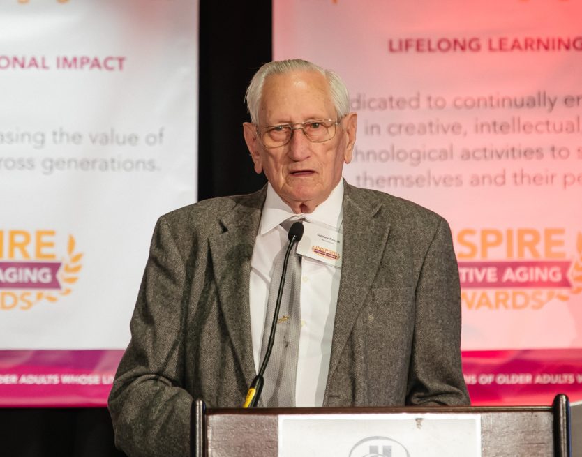 Sidney "Sid" Rouse, who received the Sound Generations Inspire Positive Aging Award for Community Service stands at a podium at the IPAA gala as he gives a speech giving thanks and reflecting upon the community service that he has offered for the past eight years, five days a week. Learn more about senior services in Seattle provided by Sound Generations, supporting older adults and their loved ones throughout the area.