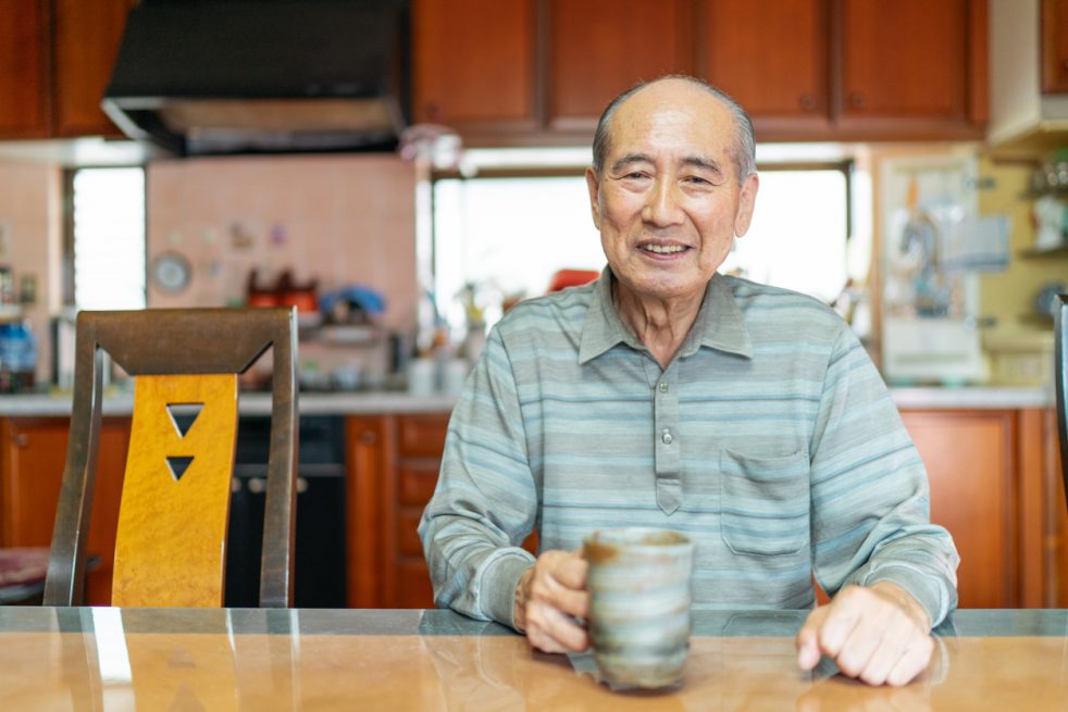 A portrait of a happy senior man while holding a coffee mug at home