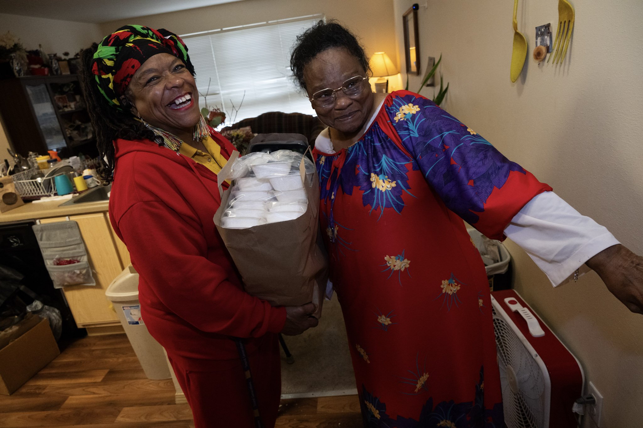 a Meals on Wheels driver and client smile together over a bag of deliveries